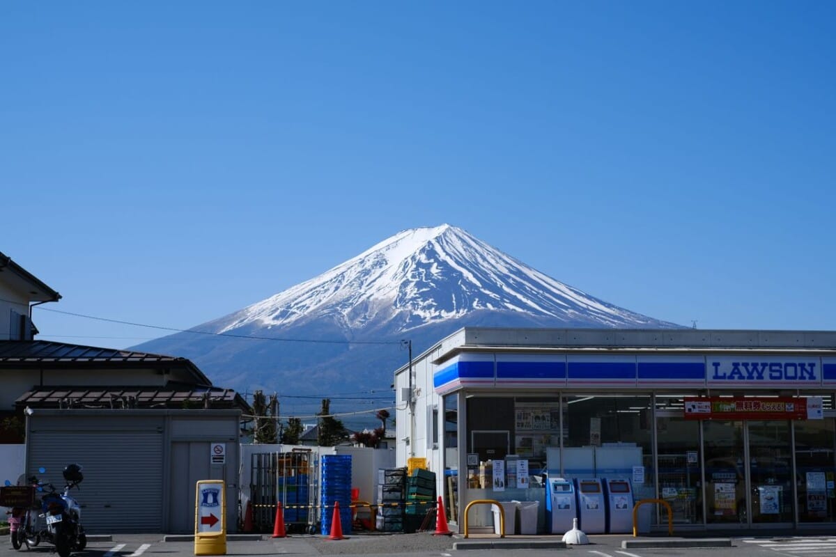 Scenic view of Mount Fuji behind a convenience store under a clear blue sky.