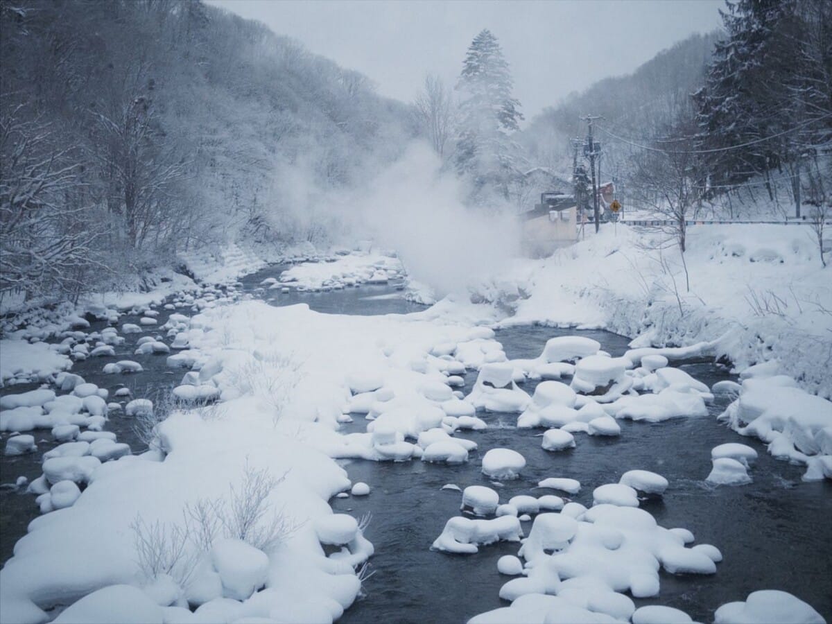 Peaceful snowy river landscape with steam rising in a tranquil winter setting.