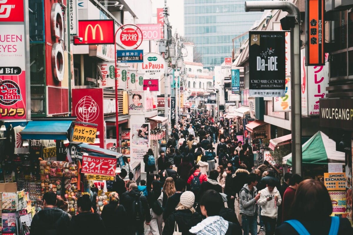 Vibrant daytime street market in Tokyo, crowded with shoppers and colorful signage.